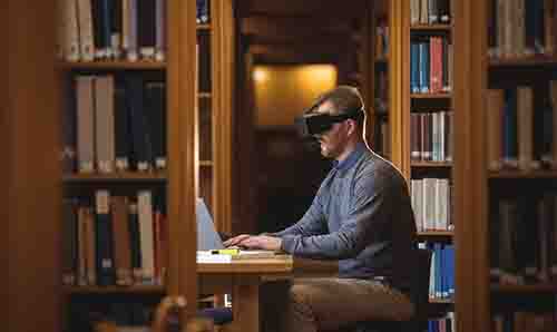 Male researcher in library wearing virtual reality headset.
